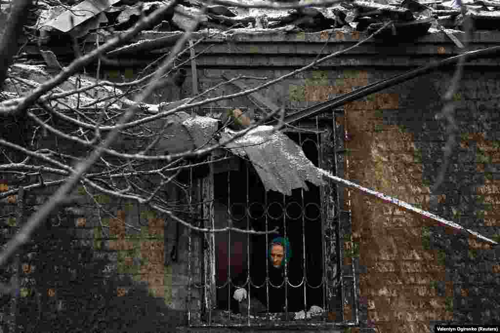 Киевлянка Надя Матвиенко моет разбитое окно своего дома, поврежденного российским ракетным ударом по Киеву.
