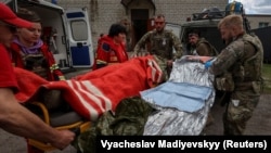 Медицинские работники и военнослужащие оказывают помощь раненому украинскому военному недалеко от города Волчанск в Харьковской области, 12 мая 2024 года
