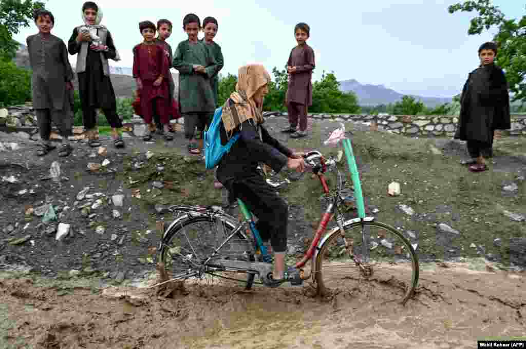 An Afghan boy rides his bicycle through rainwater along a road in the Tangi Valley of the Saydabad district in Maidan Wardak Province.
