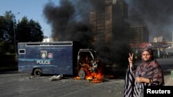 Žena stoji pored policijskog vozila kojeg su zapalili demonstranti, Karači, 9. maj 2023.