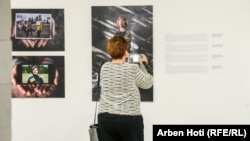 A woman photographs one of the exhibits that presents firsthand accounts in the Albanian, Serbian, English, and Ukranian languages.