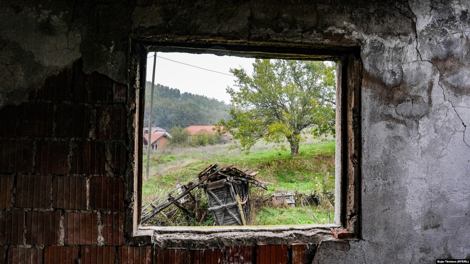 Lëndina ku u vranë civilët shqiptarë të fshatit Landovicë shihet nga dritarja e shtëpisë së dëmtuar gjatë sulmit të forcave serbe në luftën e vitit 1999.