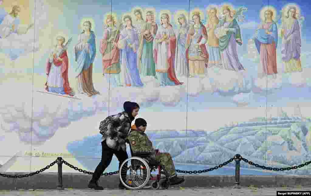 A girl pushes a disabled soldier in a wheelchair in front of frescoes of St. Michael&#39;s Golden-Domed Cathedral in Kyiv.