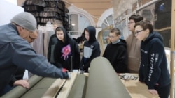 Russian schoolchildren learn to cut fabric for camouflage nets on a machine.