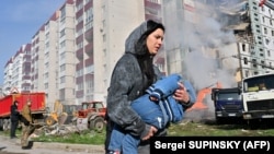 A woman carries a child past damaged residential buildings in Uman, Cherkasy region, on April 28 after Russian missile strikes targeted several Ukrainian cities overnight.
