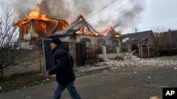 Një banor lokal largohet teksa një shtëpi e goditur nga granatimet ruse digjet në Herson të Ukrainës. Janar, 2023.
