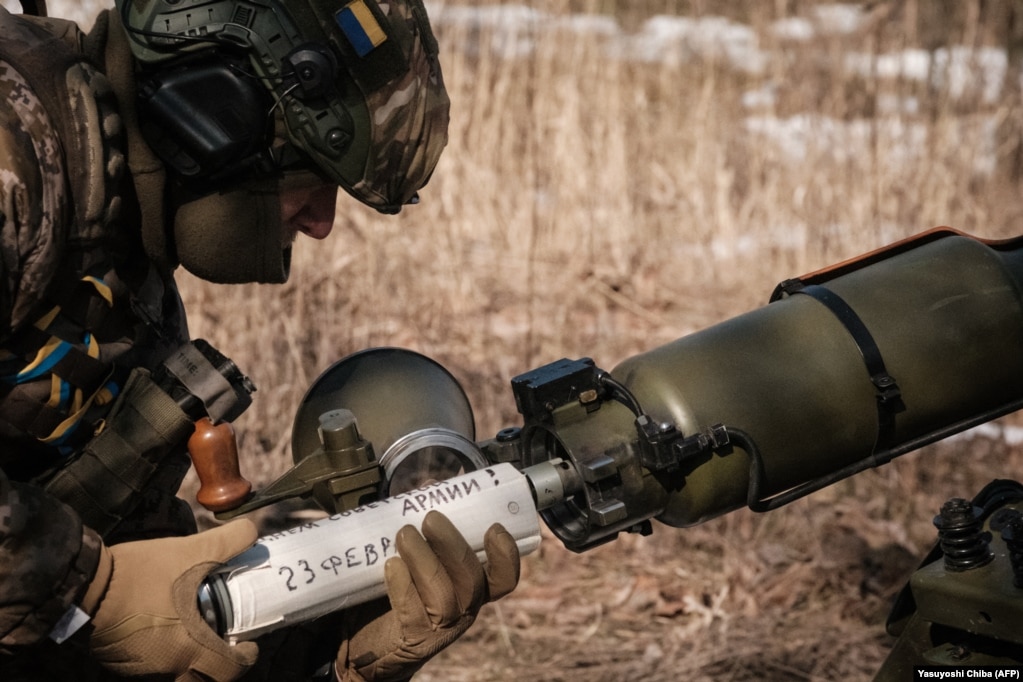 Një ushtar ukrainas duke futur një predhë në një armë afër Bahmutit në shkurt të vitit 2023. Ngarkesa shtytëse përmban mesazhin sarkastik &ldquo;Gëzuar ditën e Ushtrisë Sovjetike! 23 shkurt&rdquo;. Iryna Rybakova, një oficere e mediave në ushtrinë ukrainase i tha Radios Evropa e Lirë se mesazhe të tilla -- të cilat do të shpërthehen në copa të palexueshme -- bëhen kryesisht për konsum të mediave sociale.
