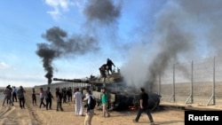 Палестинцы реагируют на горящий израильский военный автомобиль во время атаки палестинских боевиков, проникших в районы на израильской стороне границы с сектором Газа, 7 октября 2023 года