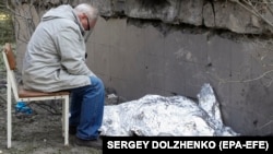 A relative sits next to the covered body of a young Ukrainian girl who was killed in a Russian missile strike on Kyiv on June 1. 