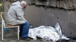 A relative sits next to the covered body of a young Ukrainian girl who was killed in a Russian missile strike on Kyiv on June 1. 
