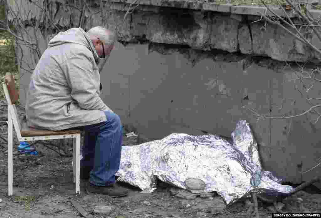 A relative sits next to the covered body of a 9-year-Ukrainian old girl, who was killed in a Russian missile strike on Kyiv.&nbsp;