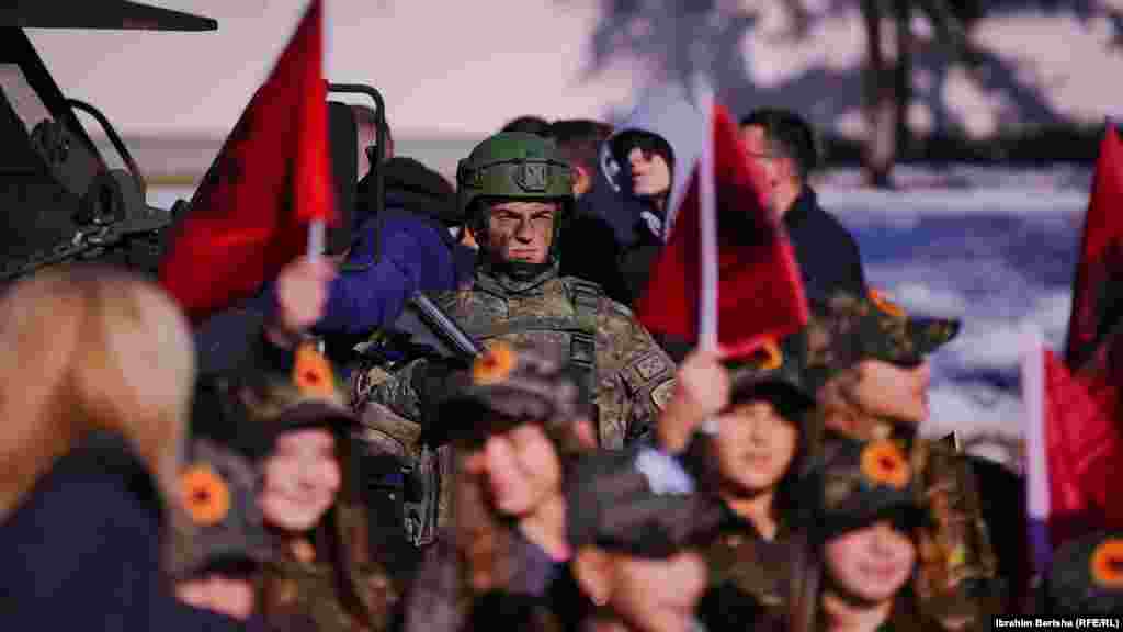Një pjesëtar i Forcës së Sigurisë së Kosovës i rrethuar nga fëmijë të veshur me uniforma.