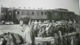 Кулакка тартылып, сүргүнгө айдоо учуру. Сүрөттөн жүк ташуучу вагондорду дагы көрүүгө болот. Автору Элла Маяйр.