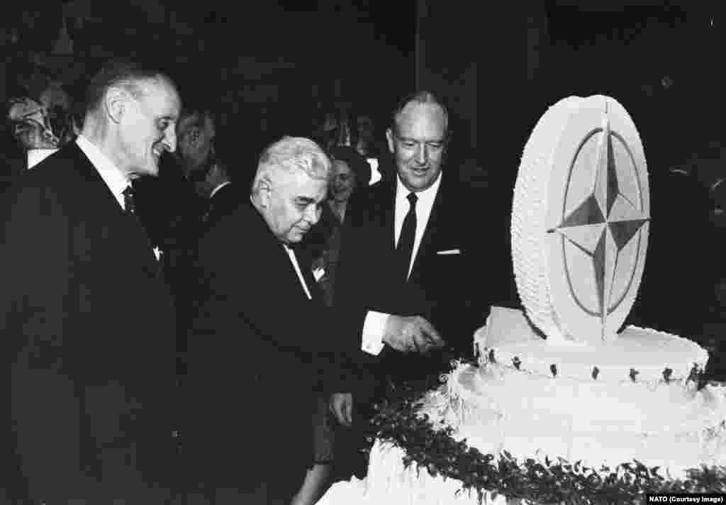 NATO Secretary-General Manlio Brosio (left) and U.S. Secretary of State William Rogers watch Icelandic Prime Minister Bjarni Benediktsson cut a NATO-themed cake during celebrations of the alliance&rsquo;s 20th anniversary in Washington D.C. in 1969.