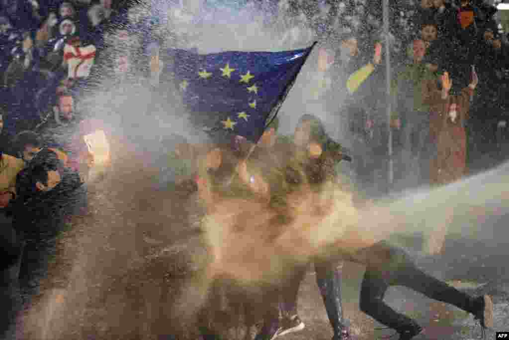Protesters brandishing a European Union flag are sprayed by a water cnanon during clashes with riot police near the Georgian parliament in Tbilisi on March 7 as thousands of demonstrators took to the streets of the capital to oppose the controversial &quot;foreign agents&quot; bill.