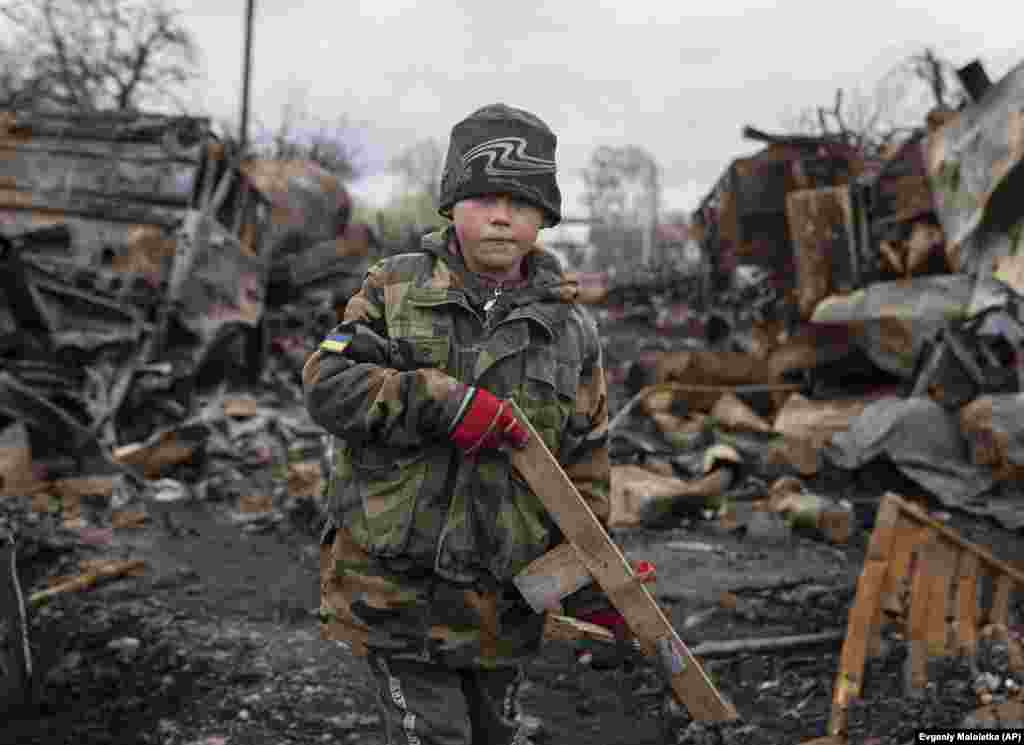 Seven-year-old Yehor holds a homemade toy rifle equipped with a &quot;sight&quot; made from a plastic bottle cap near Chernihiv on April 17. In the background is the wreckage of destroyed Russian military vehicles.&nbsp;