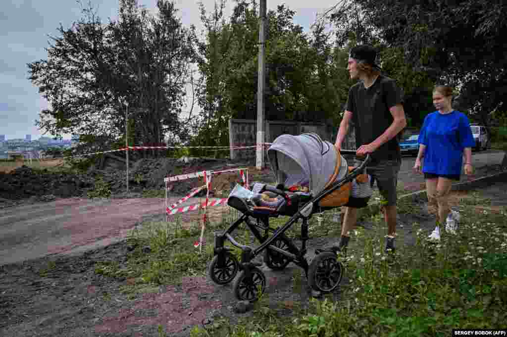 A family pushes a baby carriage past a crater after a missile strike on the city of Kharkiv on August 3.&nbsp;Russian artillery continues to pound the shattered city, adding more misery to its inhabitants, many of whom have been&nbsp;forced to live for months underground. &nbsp;
