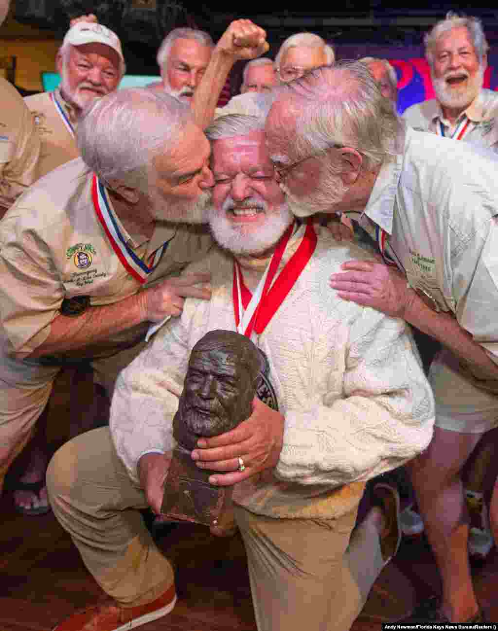 Jon Auvil reaguje dok prima čestitke od Joea Maxeya, pobjednika 2019., i Freda Johnsona, koji je pobijedio 1986., nakon pobjede na ovogodišnjem takmičenju za najsličniji izgled piscu Ernestu Hemingwayju, u Sloppy Joe's Baru u Key Westu, SAD, 2023. juli. Hemingway je živio i pisao u Key Westu tokom većeg dijela 1930-ih godina.