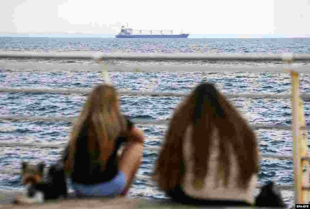 People watch as the Razoni, the first ship loaded with Ukrainian grain to set off from a Ukrainian port since the beginning of the Russian invasion, departs from Odesa on August 1. Moscow and Kyiv agreed on a deal brokered last month by Turkey and the United Nations to resume shipments of wheat and other grain from three Ukrainian ports for the first time since Russia invaded in February.