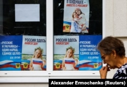 Egy nő sétál Herszonban július 25-én a Vlagyimir Putyin orosz elnököt idéző plakátok mellett: „Oroszország itt van – örökre. Az oroszok és az ukránok egy nép, egységes egész”