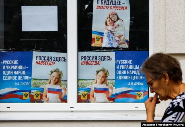 Женщина идет мимо плакатов с цитатой президента России Владимира Путина: «Русские и украинцы — один народ, единое целое». Херсон, 25 июля 2022 года