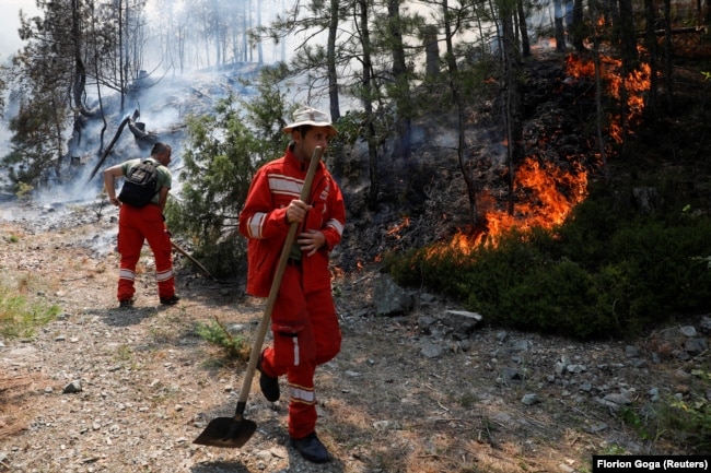 Dy zjarrfikës në Shqipëri shihen me lopata në duar në përpjekje për të shuar zjarret.
