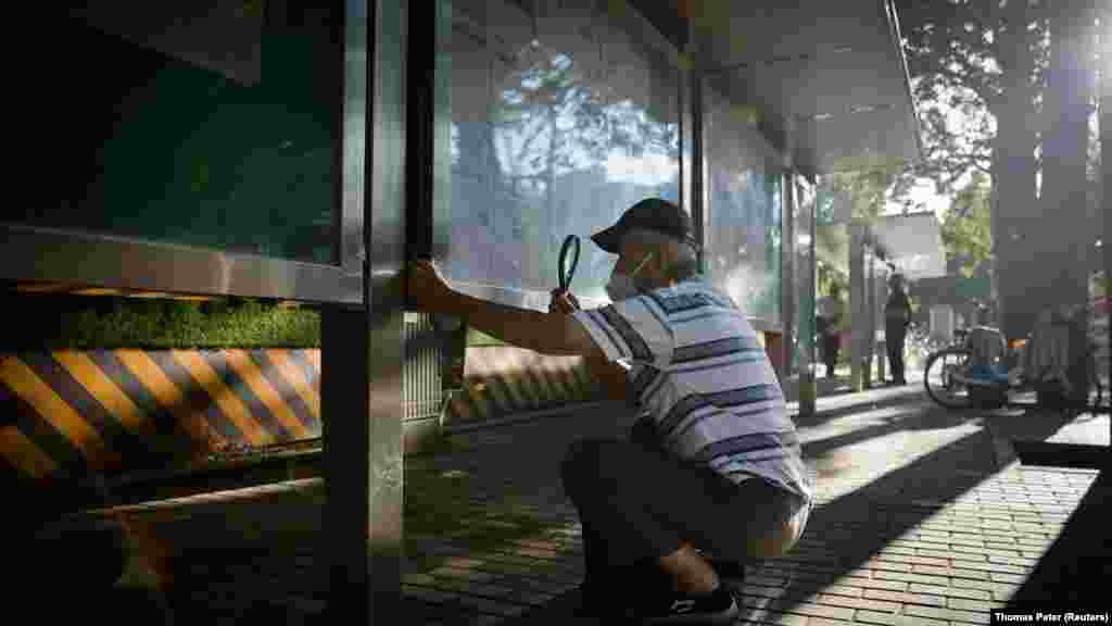 Muškarac koristi lupu da čita novine na javnom zidu u Pekingu, Kina, 28. juli.