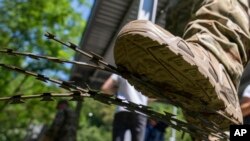 Slovenački vojnik nogom pomera žičanu ogradu podintu na granici prema Hrvatskoj na u mestu Krmačin 15. jula 2022. Ograda je izgrađena na vrhuncu migrantske krize 2015. godine.