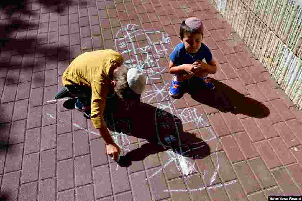 Ukrainian Hasidic Jewish refugee children draw warships and tanks on the ground with chalk.&nbsp;