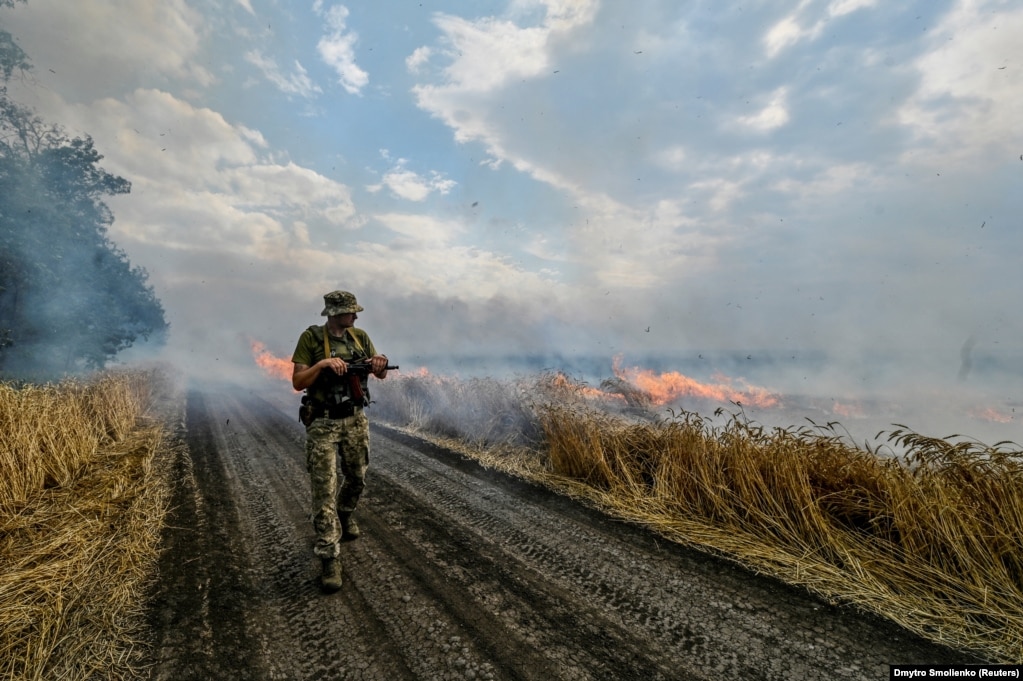 Një ushtar ukrainas kalon pranë një fushe të mbjellë me grurë e përfshirë nga flakët. Fotografia është realizuar më 17 korrik në lindje të Ukrainës, afër vijave të frontit. 