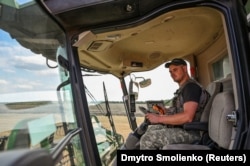 Egy mezőgazdasági munkás golyóálló mellényben vezeti a kombájnt Zaporizzsja régióban 2022. július 29-én