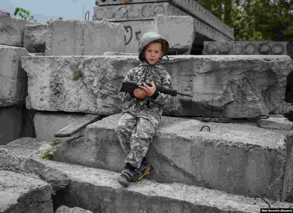 Valentyn, 6, is equipped with a helmet, toy gun, and military-style tracksuit&nbsp; in Stoyanka on May 22.&nbsp;