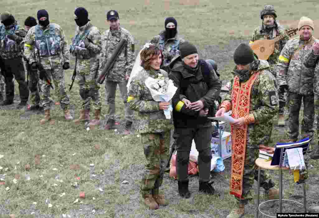 Leszja Ivascsenko és Valerij Filimonov &ndash; mindketten az ukrán Területi Védelmi Erők tagjai &ndash; a szertartást vezető lelkészt hallgatja esküvőjükön egy kijevi ellenőrző ponton március 6-án