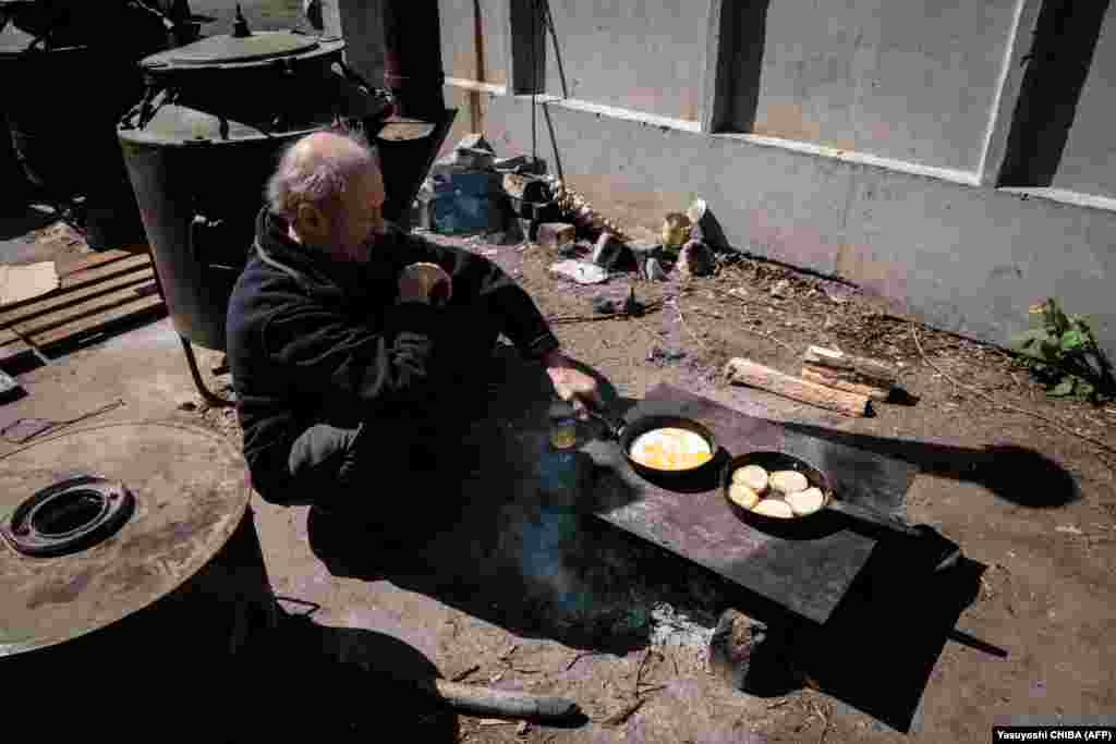 Egy idős férfi főz a menedékül szolgáló épület udvarán Szeverodonyeckben április 27-én. Mivel a súlyos harcok helyszínén az infrastruktúra is elpusztult, a helyiek általában az udvaron vagy az utcán főznek