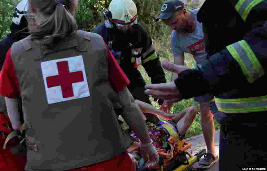 Рятувальники ДСНС, зокрема пожежники, перевозять жінку, яка зазнала поранень під час російських обстрілів жилого мікрорайону Харкова, фото від 27 червня 2022 року