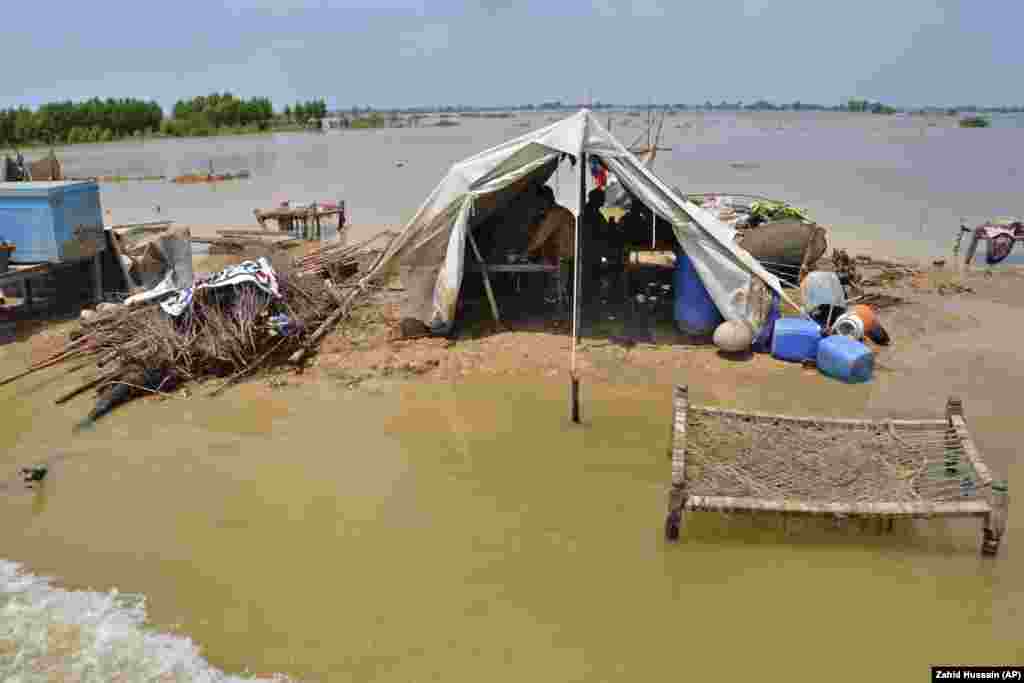 A family sits under a tent set up next to their demolished house, surrounded by floodwater, in Pakistan&#39;s southwestern Balochistan Province.