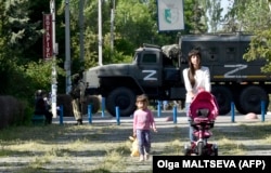 A woman and a child walk in a park as Russian servicemen patrol in Skadovsk in the Kherson region in occupied Ukraine.