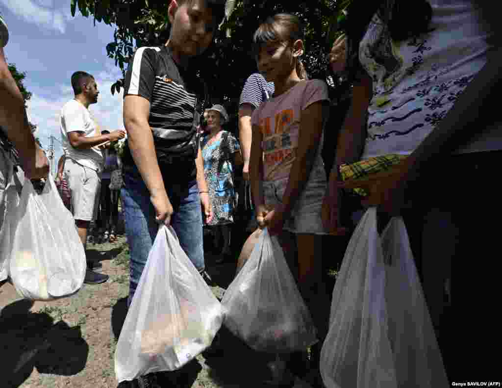 Helyi lakosok veszik át a Hub Vokzal jótékonysági szervezet által kiosztott élelmiszert tartalmazó zacskókat Merefa városában, Harkiv közelében