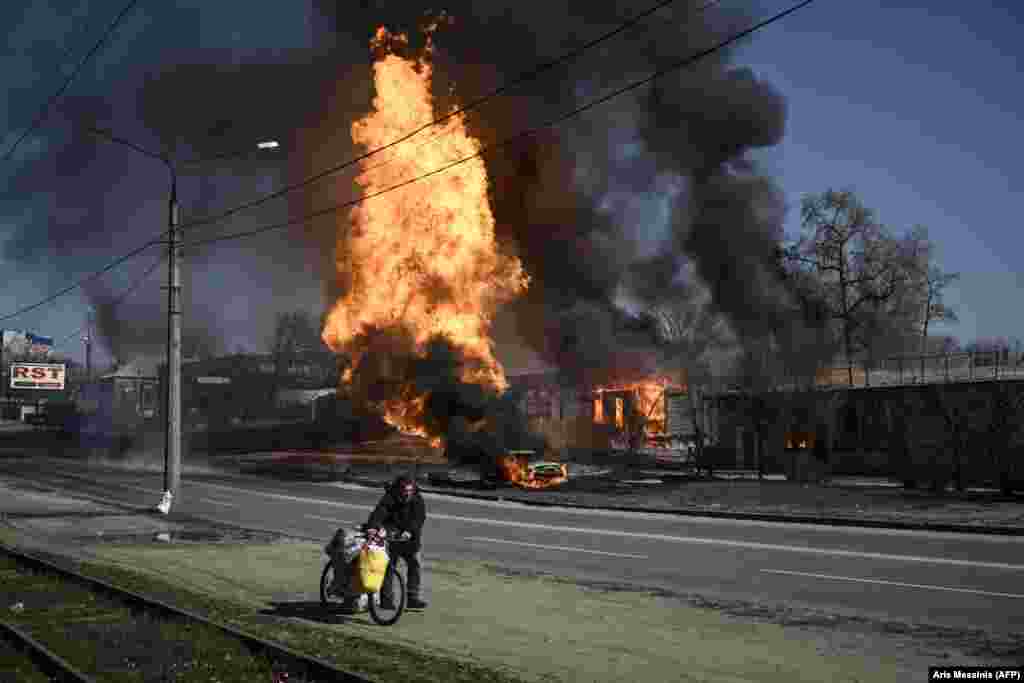 Egy épület lángol egy kerékpárral menekülő férfi mögött Harkivban március 25-én
