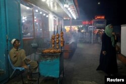 Egy nő sétál el egy ételárus mellett Kabulban (archív fotó)