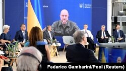 Прем’єр-міністр України Денис Шмигаль (на екрані) під час зустрічі міністрів фінансів і голів центральних банків G7 у Кенігсвінтері, Німеччина, 19 травня 2022 року