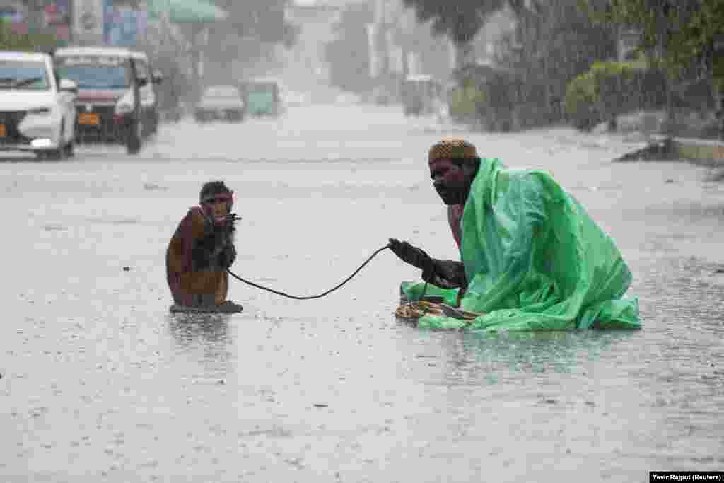 A man sits with his pet monkey as they seek charity from passersby along a road during monsoon rain in Hyderabad, Pakistan.