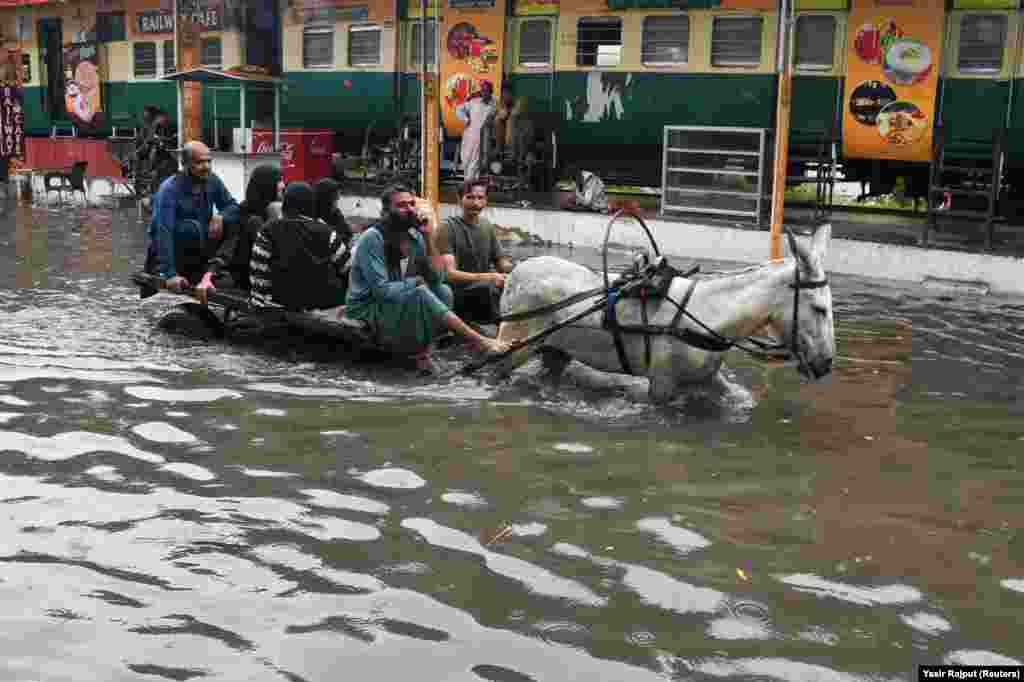 Oameni care se plimbă cu o căruță trasă de măgari pe un drum inundat, în urma ploilor din timpul sezonului musonic, în Hyderabad, Pakistan, 24 august 2022.&nbsp;