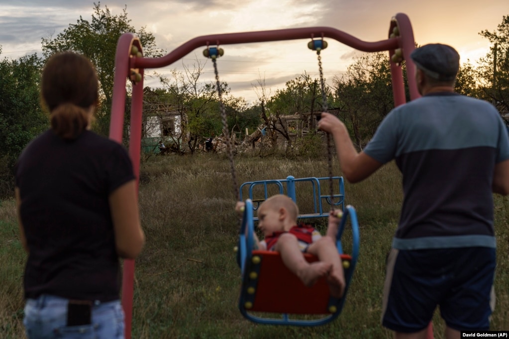 Një çift duke e luhatur fëmijën në një luhatëse pranë shtëpisë së tyre tashmë të shkatërruar nga një sulm me raketë më 16 gusht në Kramatorsk, në Ukrainën lindore.