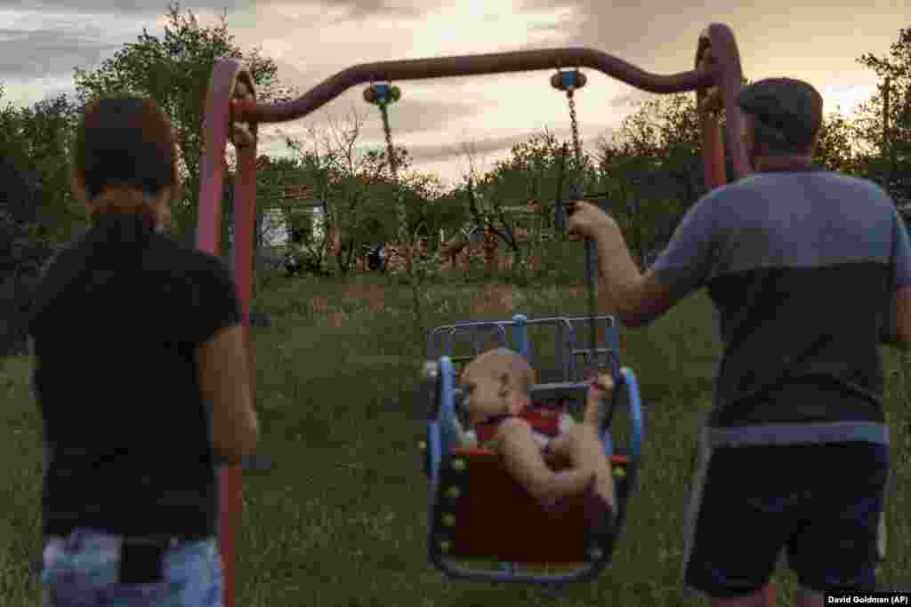 A couple push their child on a swing where a rocket attack damaged homes on August 16 in Kramatorsk, eastern Ukraine.