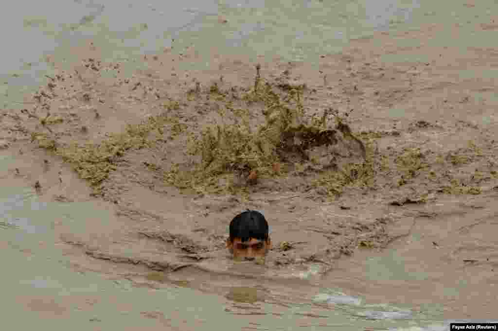 Un bărbat înoată în zonele inundate în timp ce se îndreaptă spre un teren mai înalt, în urma ploilor și inundațiilor din timpul sezonului musonic din Charsadda, Pakistan, 27 august 2022.