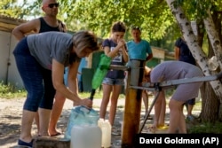 Banorët mblidhen për të nxjerrë ujë nga një pus jashtë një kompleksi apartamentesh në Sloviansk, rajoni Donjeckut, në Ukrainën lindore, 6 gusht 2022.