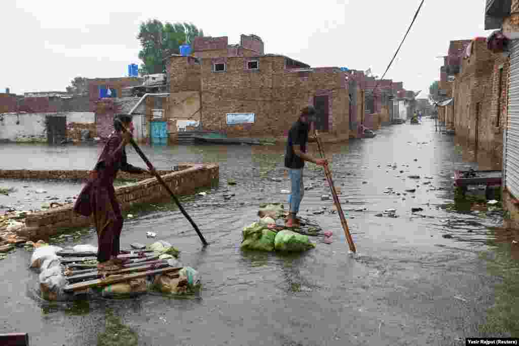Doi bărbați vâslesc pe plute improvizate în timp ce traversează o stradă inundată, pe fondul ploilor din timpul sezonului musonic din Hyderabad, Pakistan, 24 august 2022.&nbsp;