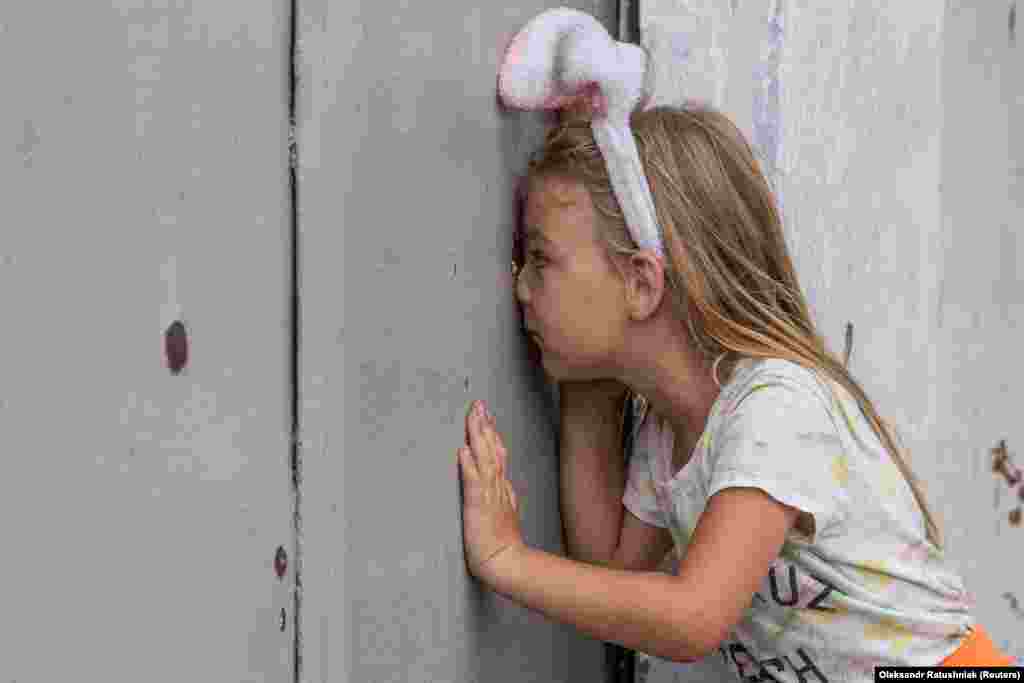 A girl looks through a shrapnel hole&nbsp; in a fence after a recent Russian military strike in Mykolayiv, Ukraine, on August 10.