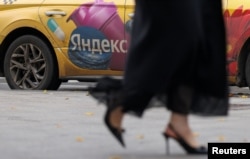 Žena u Moskvi prolazi pored taksi vozila s oznakom Yandex (arhivska fotografija)